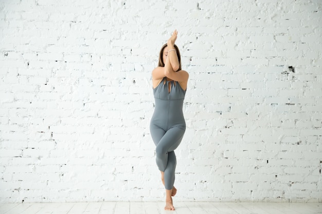 Foto grátis jovem atraente em garudasana pose, estúdio branco backgrou