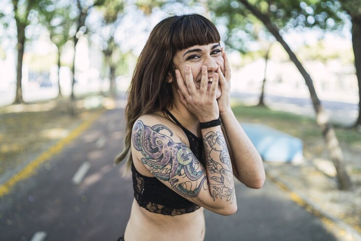 Foto grátis jovem atraente mulher branca com tatuagens em pé no parque e fazendo uma careta