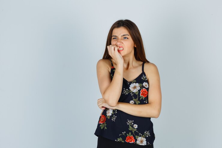 Foto grátis jovem atraente na blusa, roendo as unhas emocionalmente e parecendo nervosa, vista frontal.