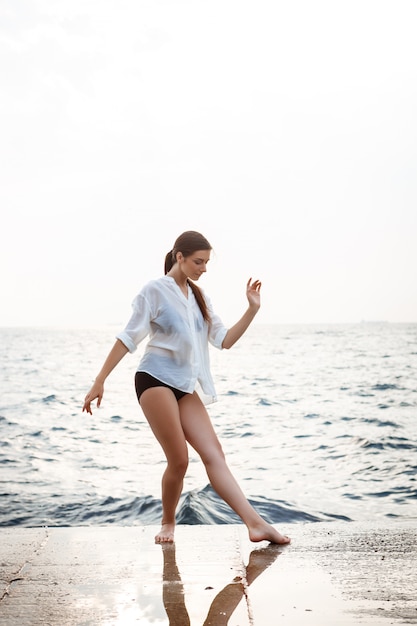 Jovem bailarina linda dançando e posando do lado de fora, parede do mar