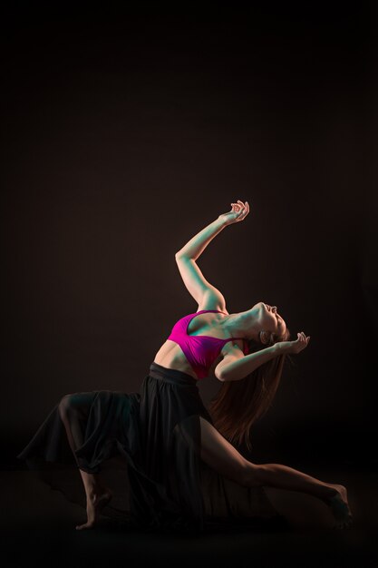 Jovem bailarina linda num vestido bege dançando na parede preta