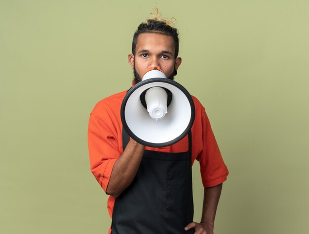 Jovem barbeiro afro-americano de uniforme falando pelo alto-falante com a mão na cintura