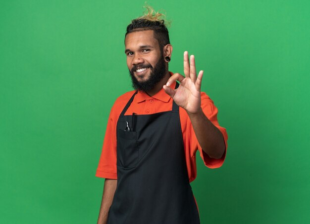 Jovem barbeiro afro-americano sorridente, usando uniforme, fazendo sinal de ok