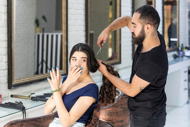 Jovem barbeiro tentando cortar todo o cabelo de seu cliente Foto de alta qualidade