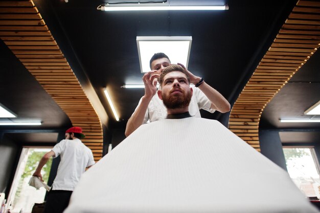 Jovem barbudo cortando o cabelo pelo cabeleireiro enquanto está sentado na cadeira na barbearia Barber soul