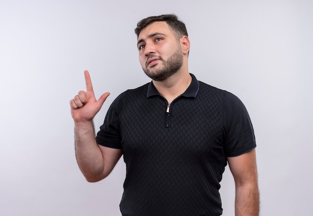 Jovem barbudo de camisa preta apontando o dedo para cima tentando se lembrar