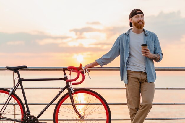 Jovem barbudo viajando de bicicleta no pôr do sol no mar