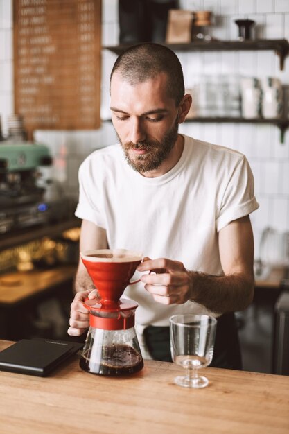 Jovem barista pensativo em pé no balcão do bar e preparando o café enquanto trabalhava no café