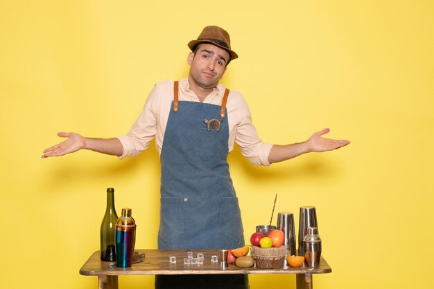 Jovem barman em frente à mesa com bebidas shakers no fundo amarelo