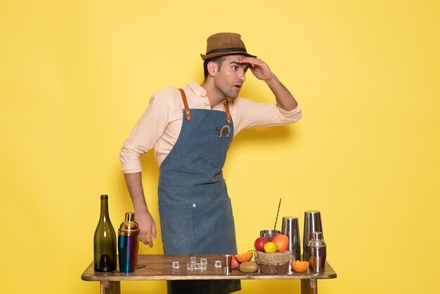 Jovem barman em frente à mesa com bebidas shakers no fundo amarelo