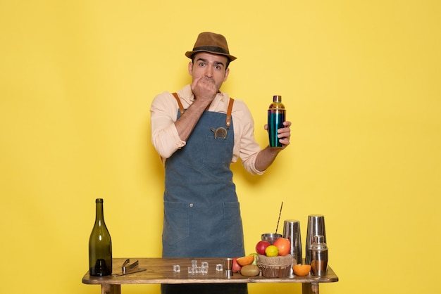 Foto grátis jovem barman masculino em frente à mesa com bebidas e coquetéis no fundo amarelo