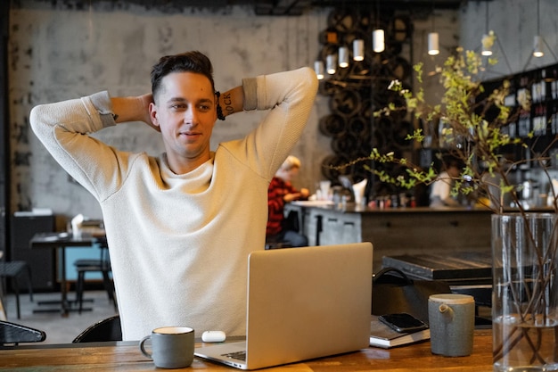 Jovem bebe chá e trabalha em um laptop, freelancer trabalhando em um café