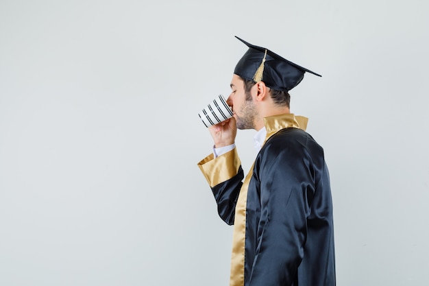 Jovem bebendo café aromático em uniforme de pós-graduação.