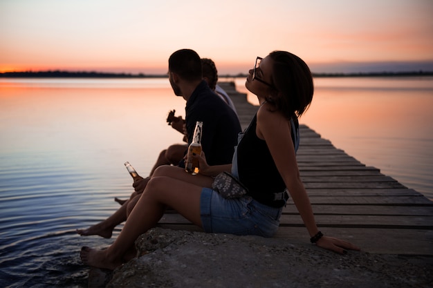 Jovem bela companhia de amigos descansando à beira-mar durante o nascer do sol