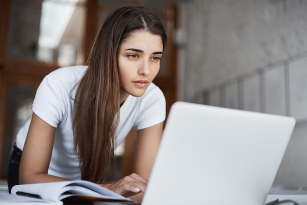 Jovem bela estudante navegando na internet em um laptop em busca de novas informações na biblioteca da Universidade.