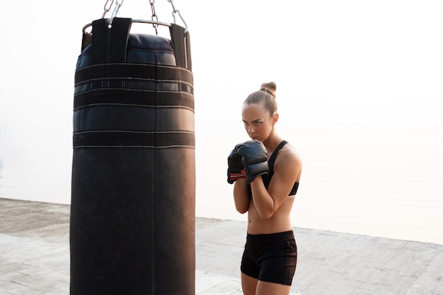 Jovem bela garota esportiva treinamento boxe à beira-mar.