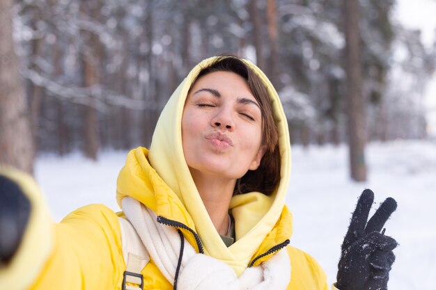 Jovem, bela mulher feliz e alegre no videoblog da floresta de inverno, faz uma foto de selfie