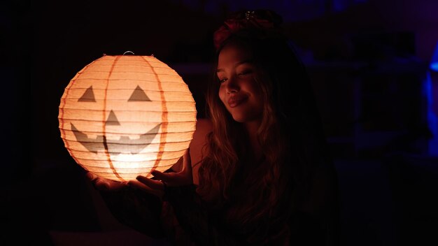 Jovem bela mulher hispânica vestindo fantasia de katrina segurando lâmpada de halloween em casa