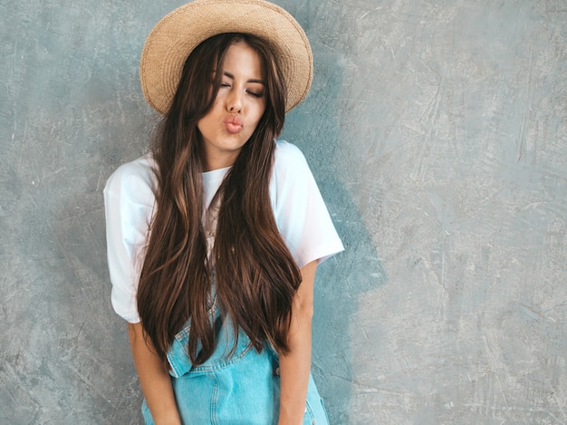 Jovem bela mulher sorridente olhando. Menina na moda em roupas de verão casual macacão e chapéu ... Fazendo cara de pato