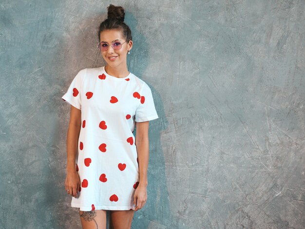 Jovem bela mulher sorridente olhando. Menina na moda em verão casual branco vestido e óculos de sol.