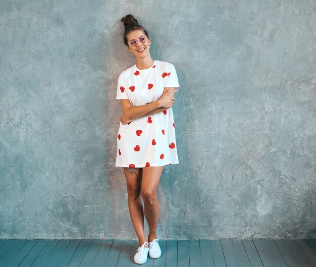 Jovem bela mulher sorridente olhando. Menina na moda em verão casual branco vestido e óculos de sol.