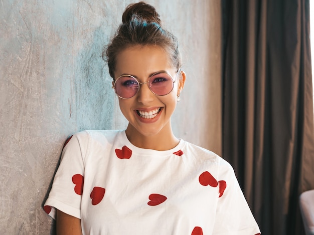 Jovem bela mulher sorridente, olhando para a câmera Menina na moda em óculos de sol e vestido casual de verão branco