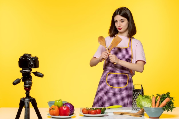 Jovem blogueira de comida em avental rosa gravando vídeo para mídias sociais com colheres de pau