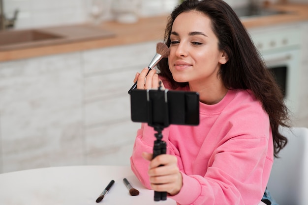 Jovem blogueira gravando a si mesma e colocando maquiagem