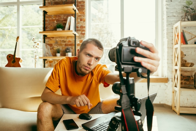 Jovem blogueiro caucasiano com câmera profissional gravando revisão de vídeo de gadgets em casa.