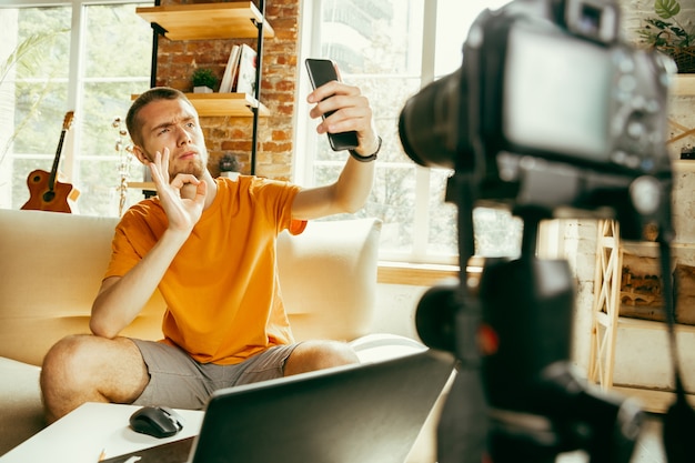 Jovem blogueiro caucasiano com câmera profissional gravando revisão de vídeo de smartphone em casa