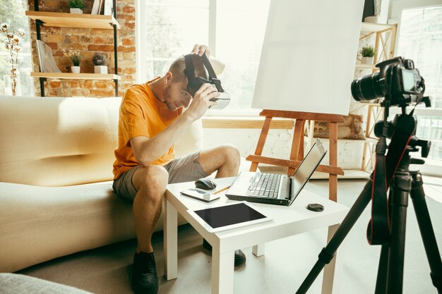 Jovem blogueiro caucasiano com equipamento profissional gravando uma análise de vídeo de óculos de realidade virtual em casa