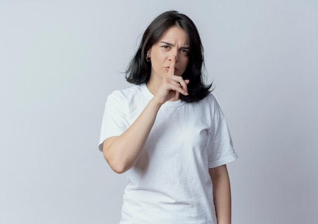 Jovem bonita caucasiana carrancuda gesticulando em silêncio para a câmera isolada no fundo branco com espaço de cópia