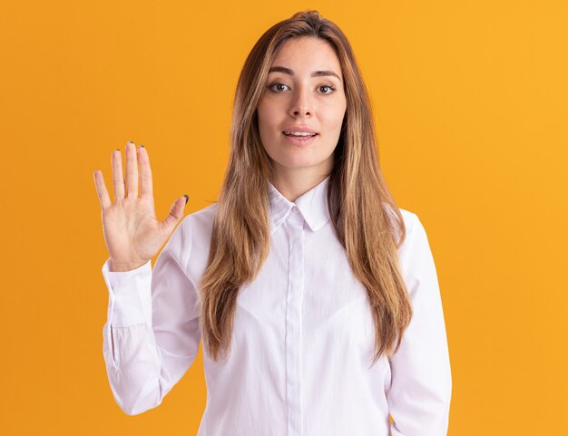 Jovem bonita caucasiana confiante em pé com a mão levantada, isolada na parede laranja com espaço de cópia