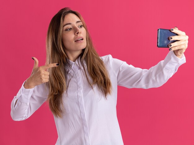 Jovem bonita caucasiana confiante olha e aponta para o telefone