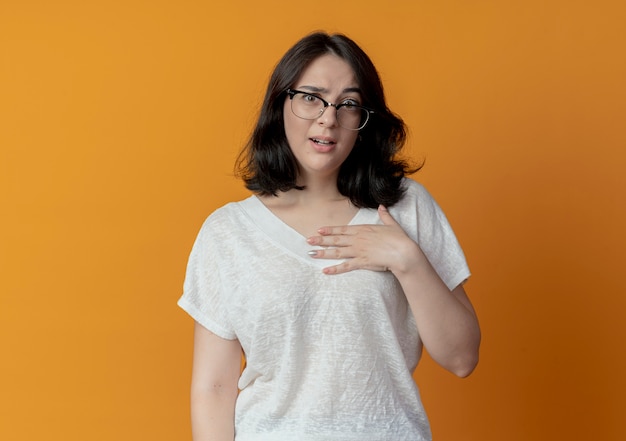 Foto grátis jovem, bonita, caucasiana, impressionada, usando óculos, colocando a mão no peito, isolada em um fundo laranja com espaço de cópia