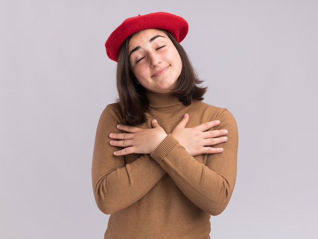 Jovem, bonita, caucasiana, satisfeita, com chapéu de boina colocando as mãos no peito