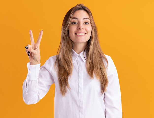 Jovem bonita caucasiana sorridente gesticulando sinal de mão da vitória isolado na parede laranja com espaço de cópia