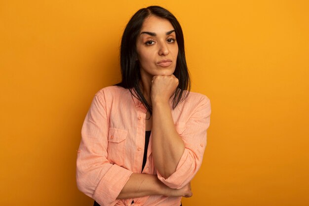 Jovem bonita confiante vestindo uma camiseta rosa colocando o punho sob o queixo isolado em amarelo com espaço de cópia