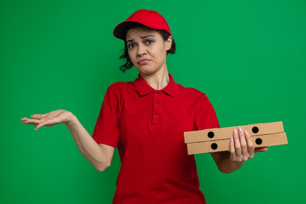 Jovem bonita confusa entregadora de pizza segurando caixas de pizza e mantendo a mão aberta