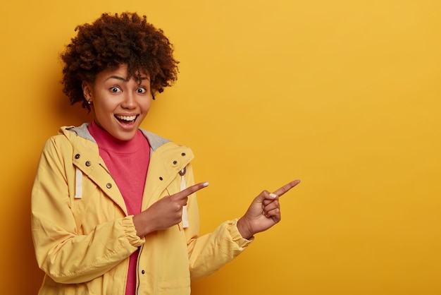 Jovem bonita de pele escura com penteado afro, sorri alegremente, anuncia algo legal e atraente