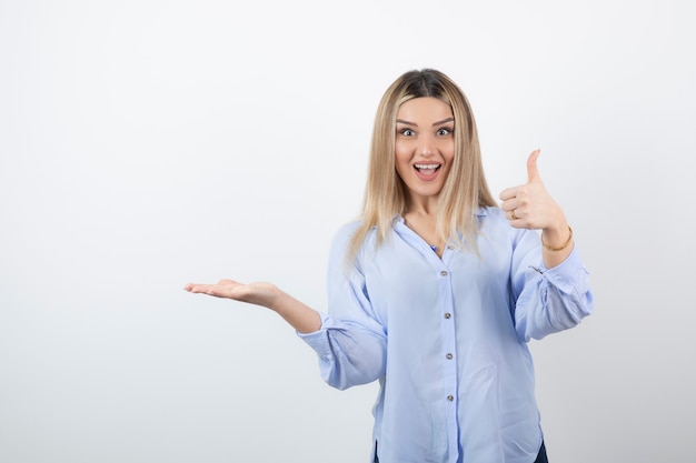 Jovem bonita em pé e desistir de polegares em fundo branco.