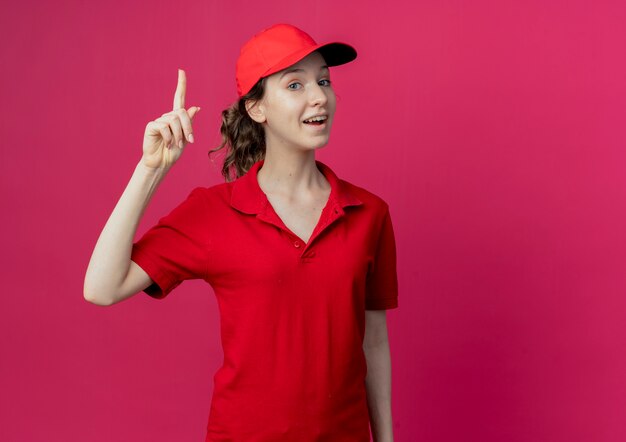 Jovem, bonita, entregadora, impressionada, com uniforme vermelho e dedo levantando a tampa, isolado em um fundo carmesim com espaço de cópia