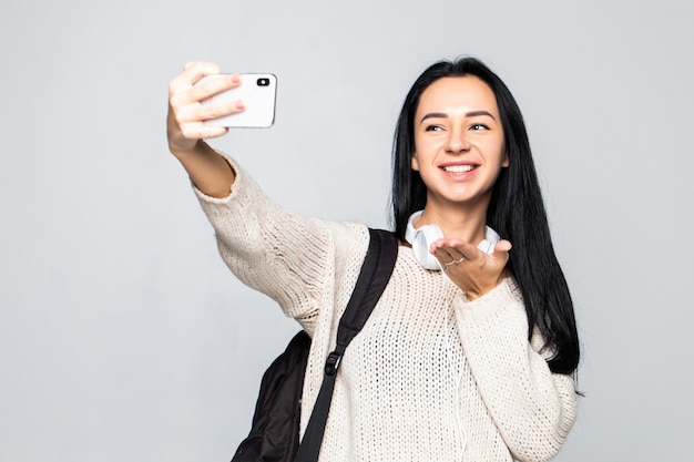 Jovem bonita feliz mandando beijo do ar e tomando selfie com smartphone parede cinza