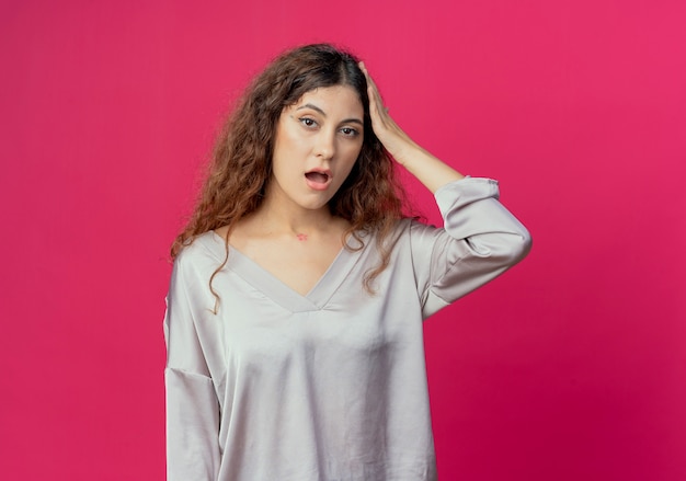 Jovem bonita impressionada colocando a mão na cabeça isolada no fundo rosa