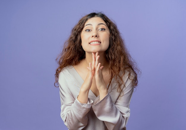 Jovem bonita sorridente colocando os dedos embaixo do queixo, isolado no azul