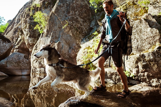 Jovem bonito andando com cães huskies no canyon perto da água