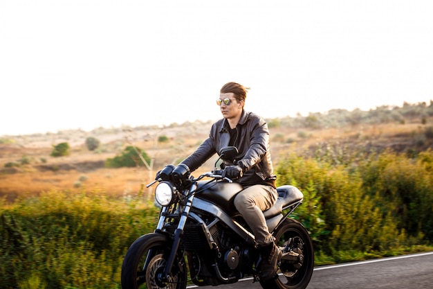 Jovem bonito andar de moto na estrada rural.