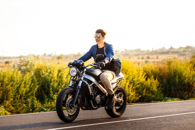 Jovem bonito andar de moto na estrada rural.