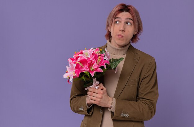 Jovem bonito ansioso segurando um buquê de flores e olhando para o lado