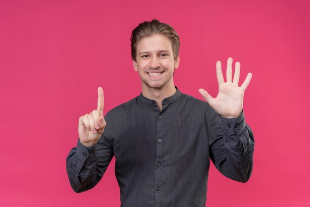 Jovem bonito aparecendo e apontando para cima com os dedos número seis